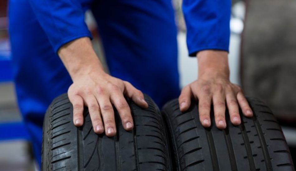 Esta imagem apresente um homem segurando pneus de diferentes tamanhos em cada uma de suas mãos