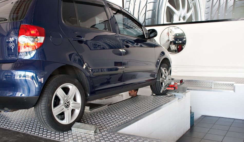 Esta imagem se refere ao serviço de alinhamento e cambagem da roda de um veículo de passeio a ser realizado em uma rampa de oficina mecânica